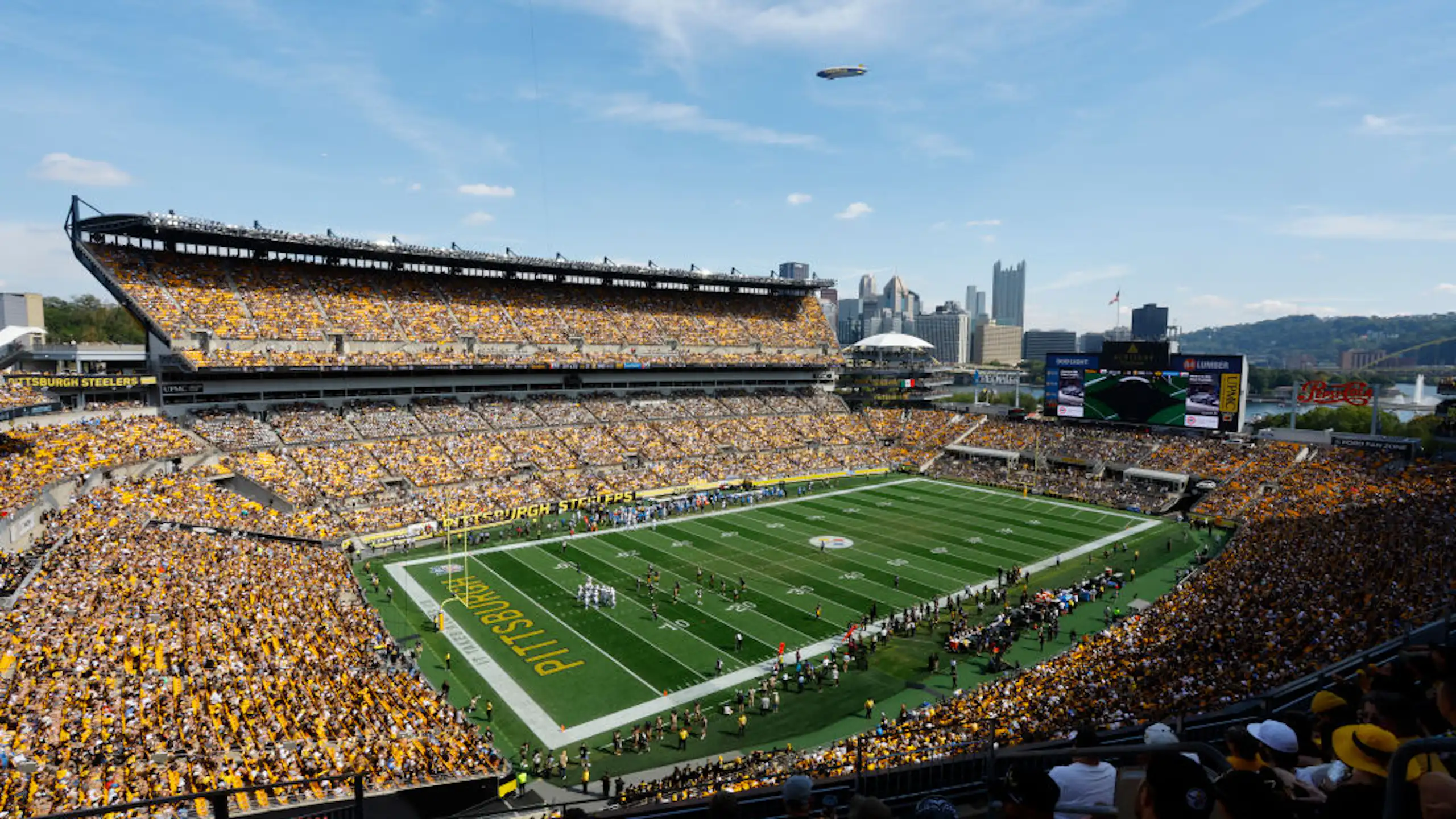 An aerial shot shows a packed football stadium with a city skyline in the background.