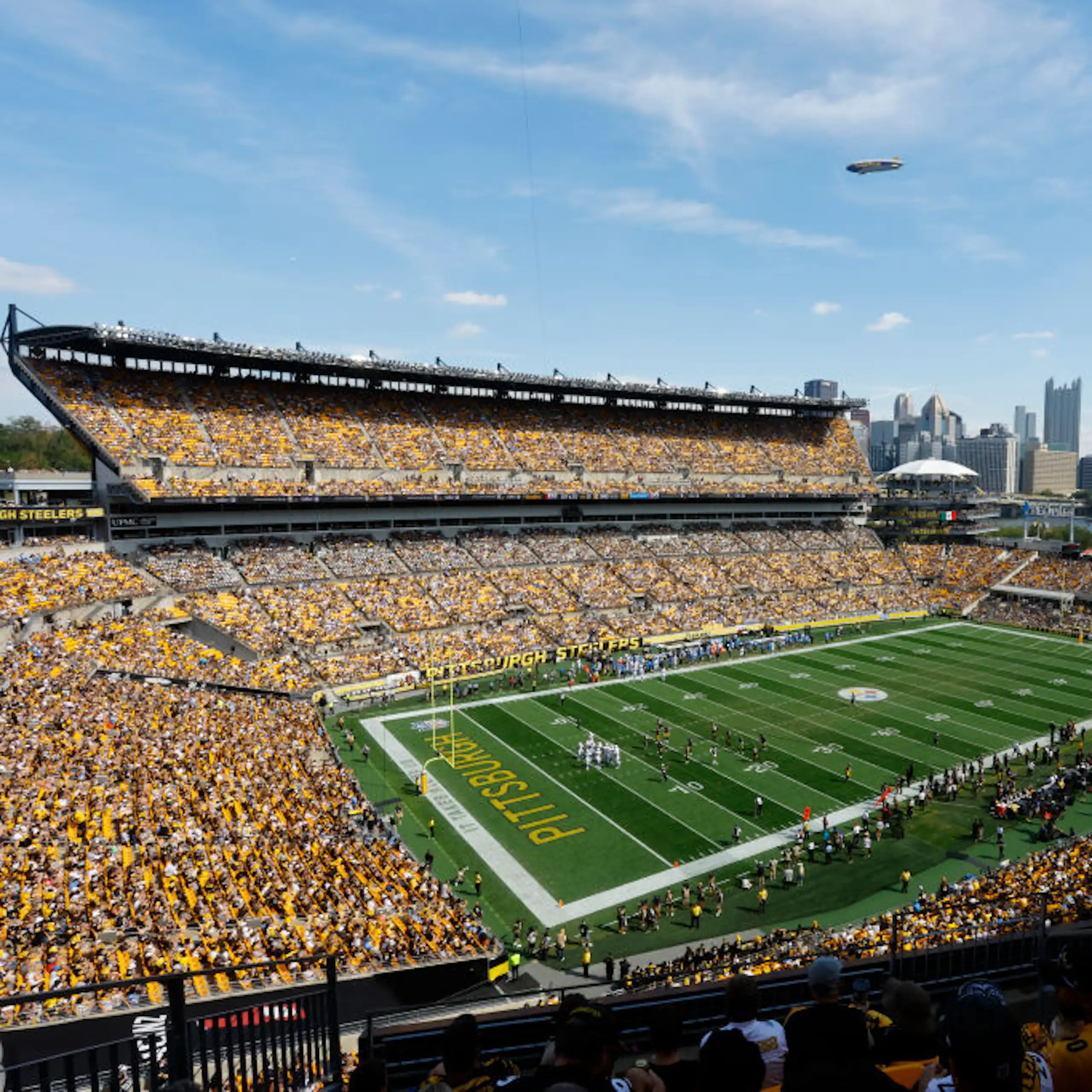 An aerial shot shows a packed football stadium with a city skyline in the background.