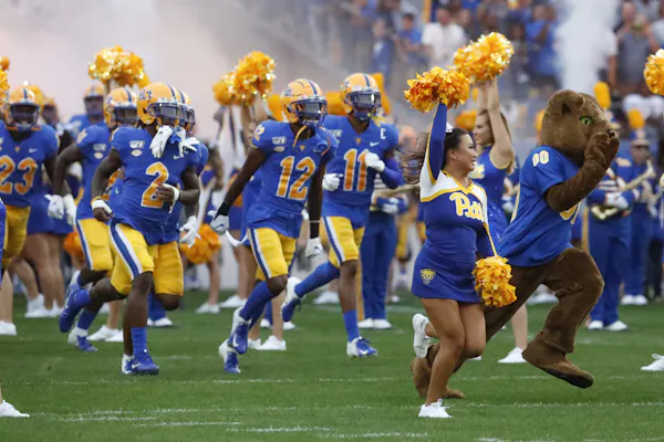 Football players and cheerleaders wearing royal blue and gold run on to a football field.