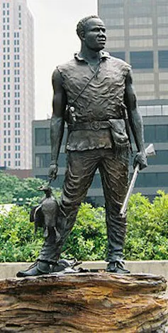 A bronze statue of a man holding a bird and a gun, looking off into the distance
