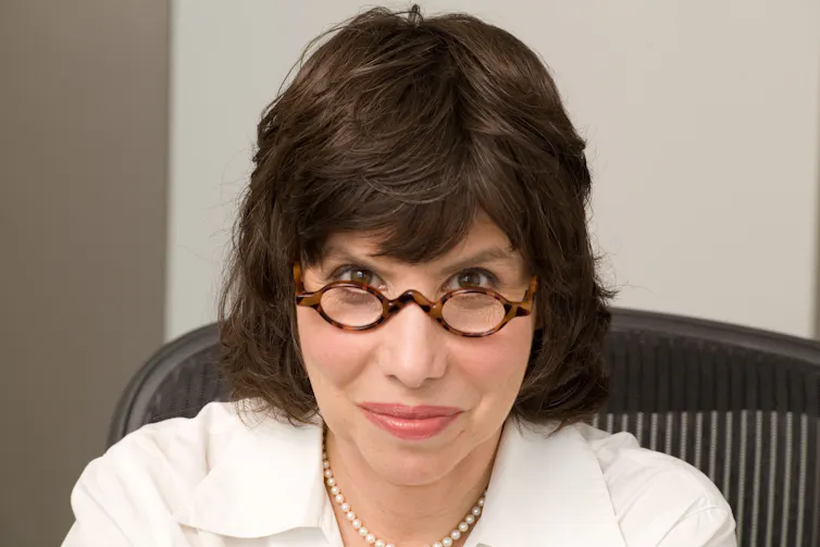 a woman in a white shirt, looking over her glasses