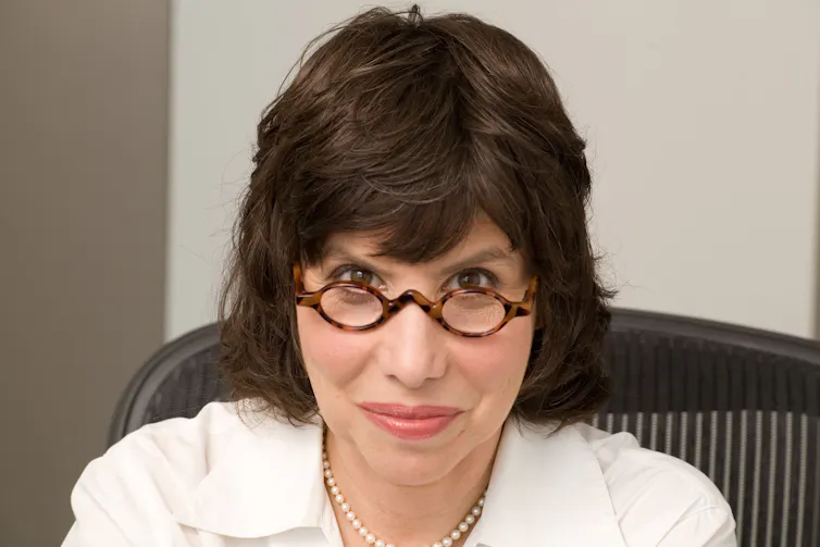 a woman in a white shirt, looking over her glasses