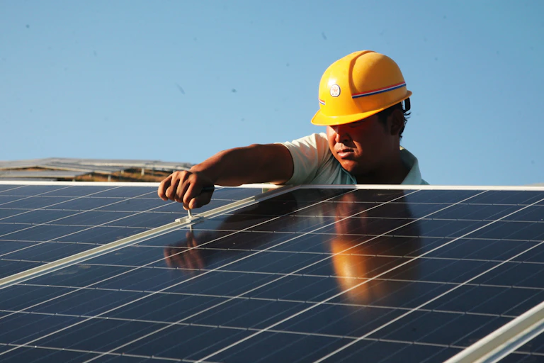 Worker with hard hat adjusts rooftop solar panels.