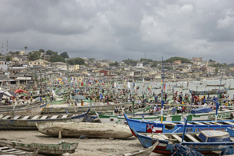 Small wooden boats lined up on the shore with over 100 people getting ready to go out to sea