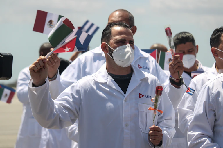 waving cuban doctors in white coats and face masks arrive back in cuba from mexico.