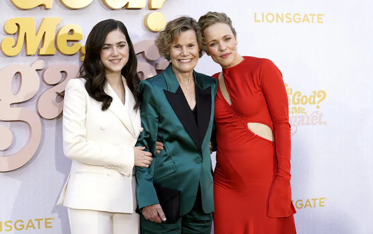 three smiling women, two in smart suits and one in a slinky red dress
