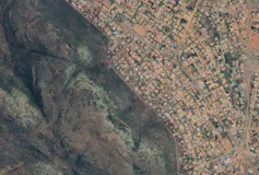 A satellite image showing houses built up to a fence of a big green nature reserve area