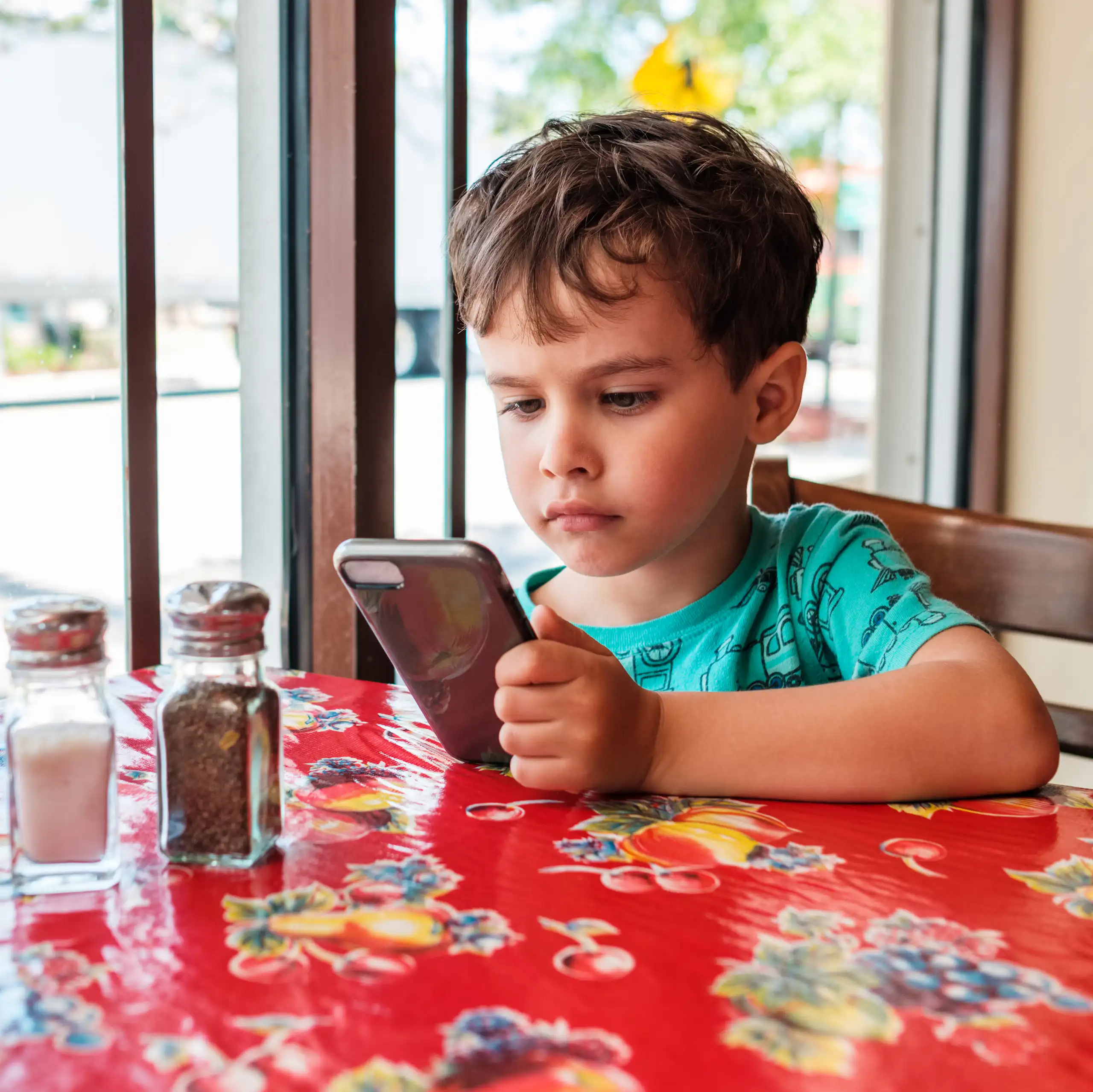 Small boy looking at phone at restaurant table