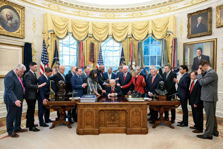 US president Donald Trump at the centre of a huddle of people who are touching him.