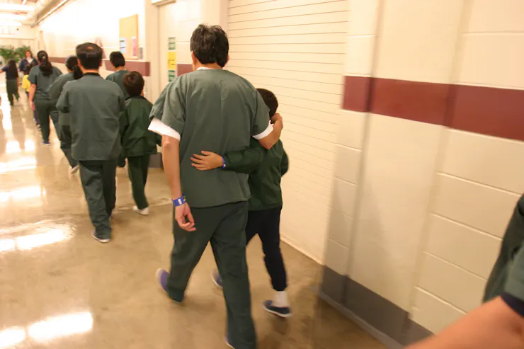 Parents and children dressed in olive green outfits walk along a brightly lit hallway.