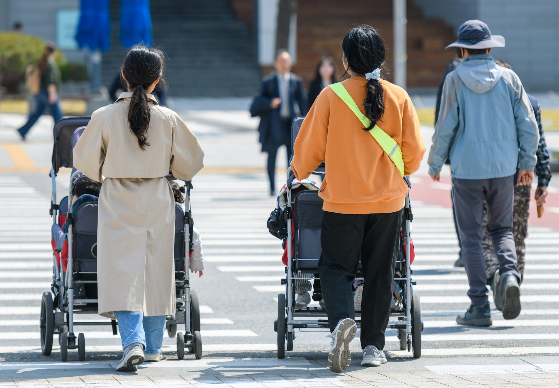Women push strollers down a street.