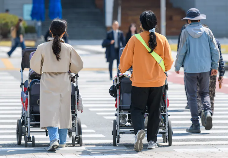 Women push strollers down a street.