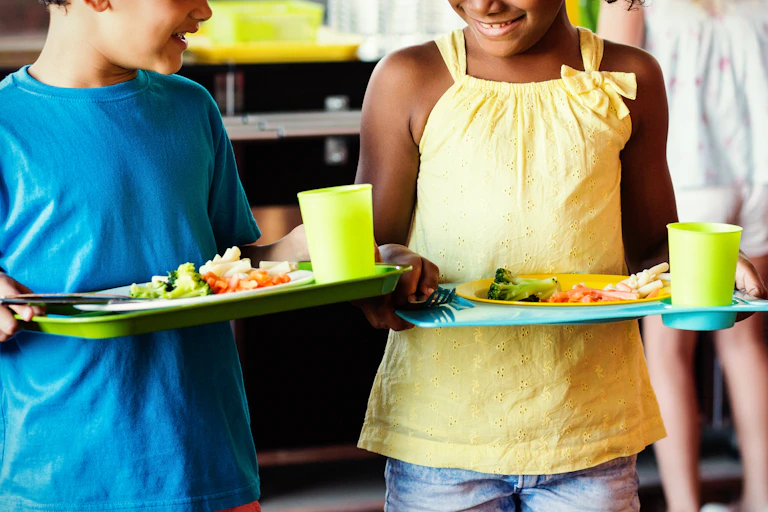 boy in blue shirt, girl in yellow T shirt, both holding trays of fresh healthy food