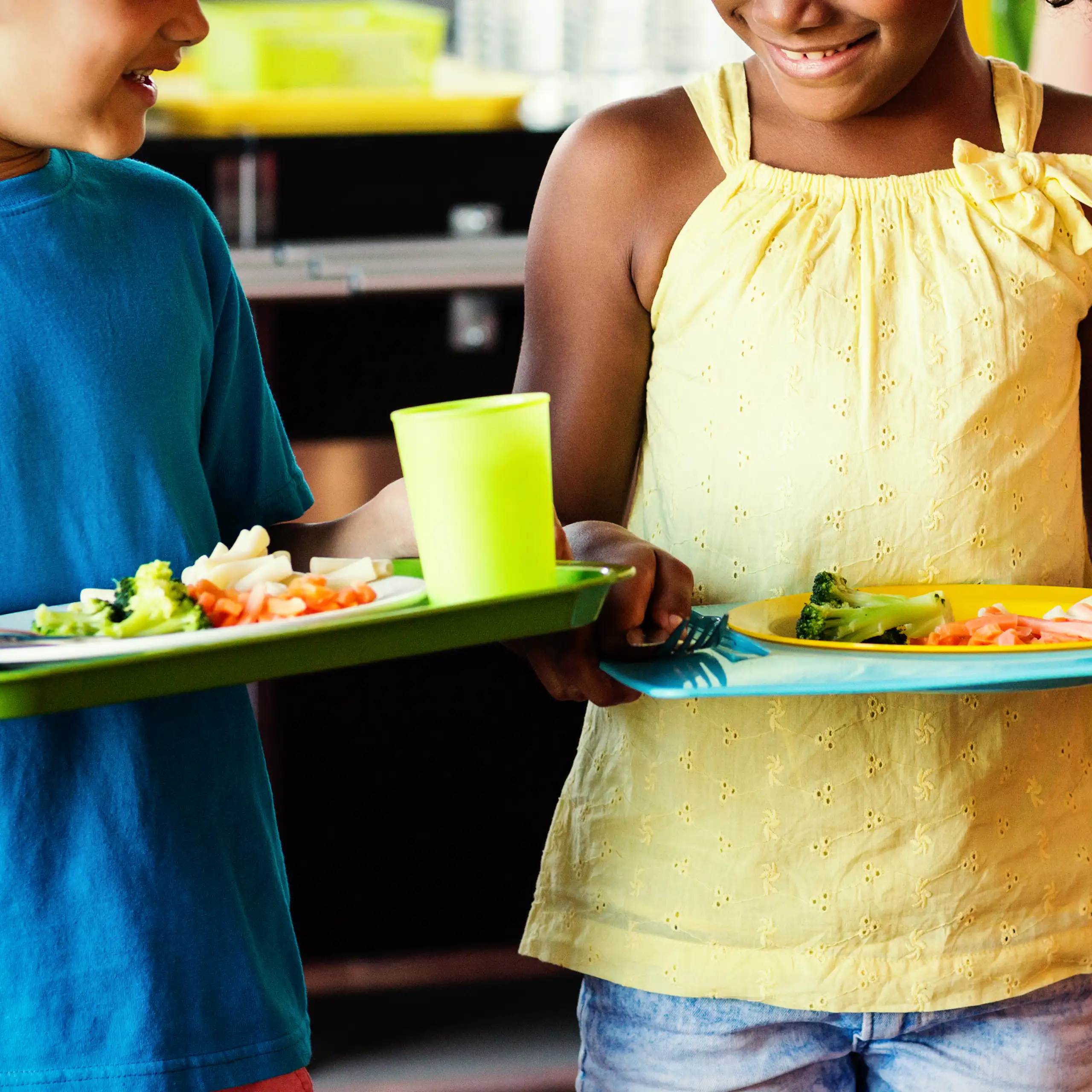 boy in blue shirt, girl in yellow T shirt, both holding trays of fresh healthy food