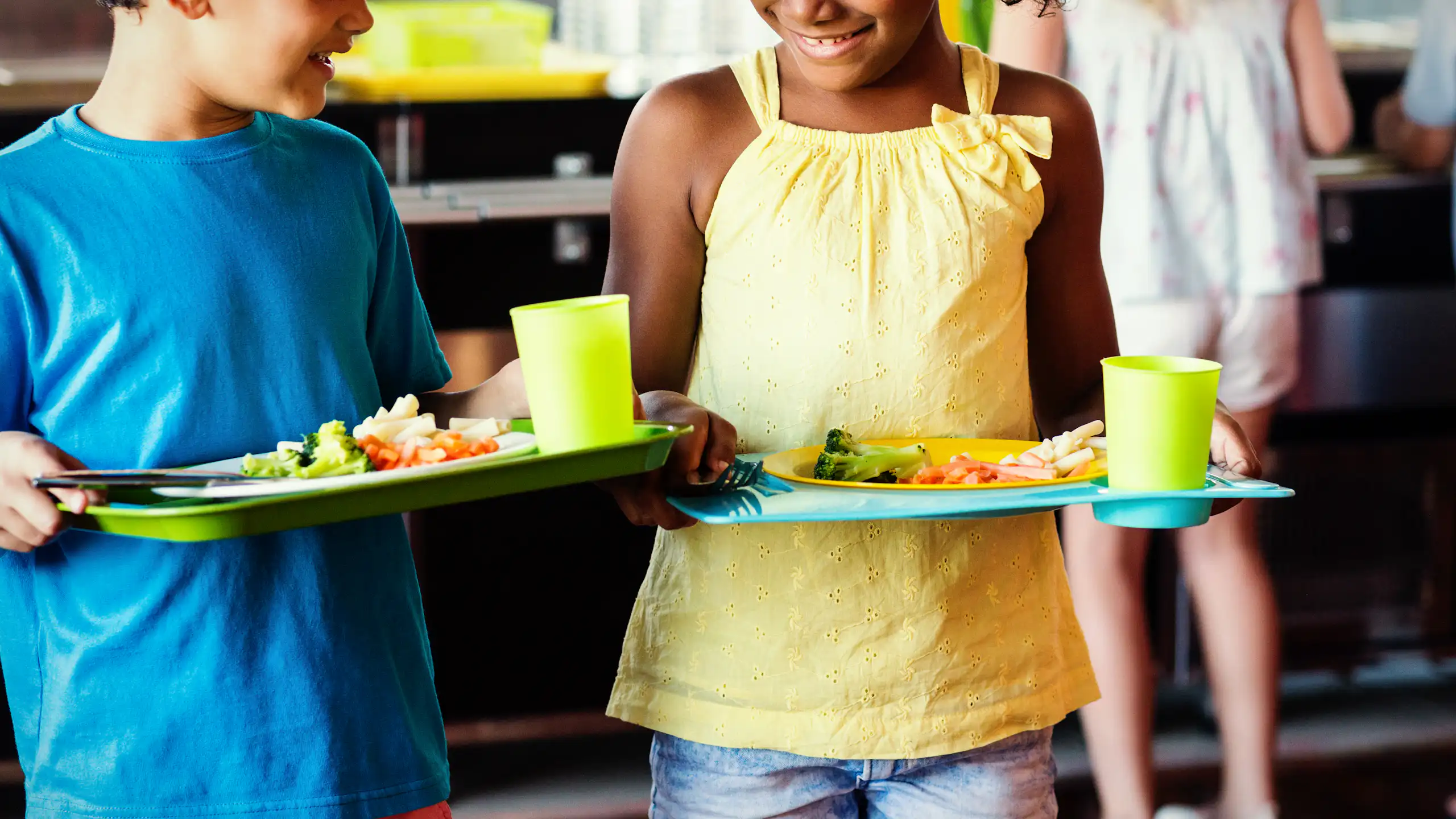 boy in blue shirt, girl in yellow T shirt, both holding trays of fresh healthy food