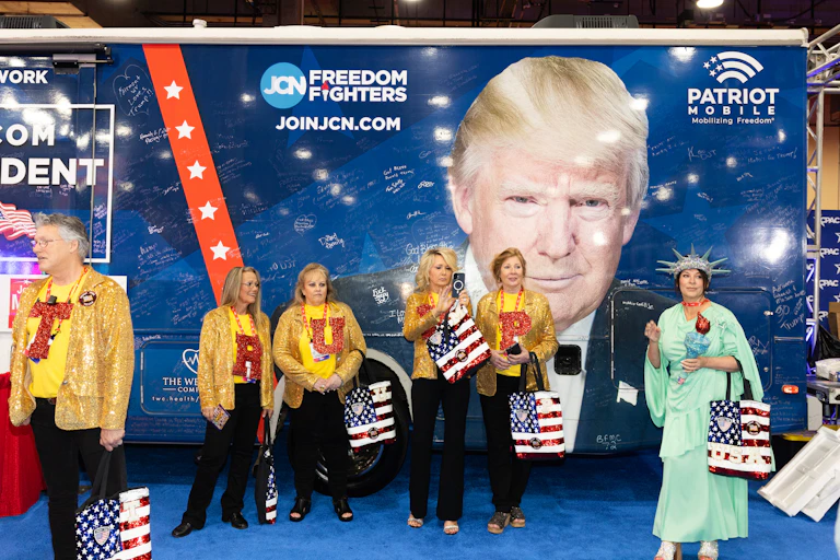 People wearing the letters that spell 'TRUMP' standing in front of a huge image of President Donald Trump.