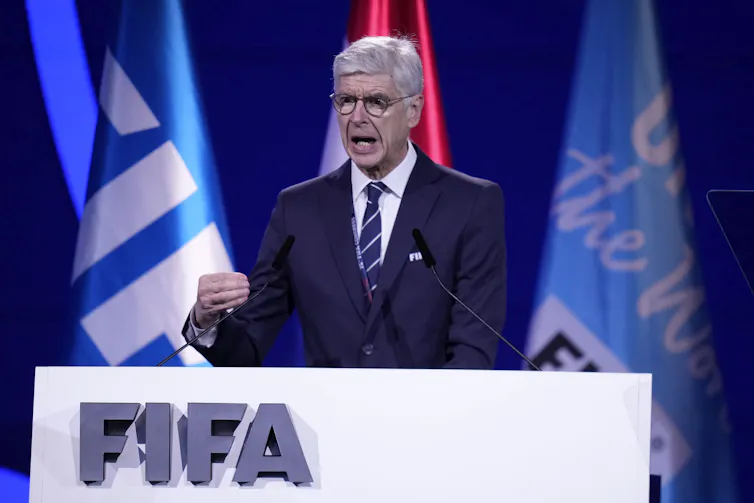 A white man in a suit speaks from behind a podium that says FIFA on it
