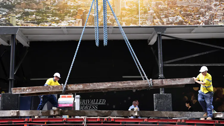 Construction workers work with a large beam