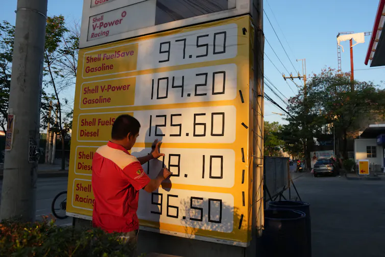 Un hombre ajusta los precios del combustible en un cartel.