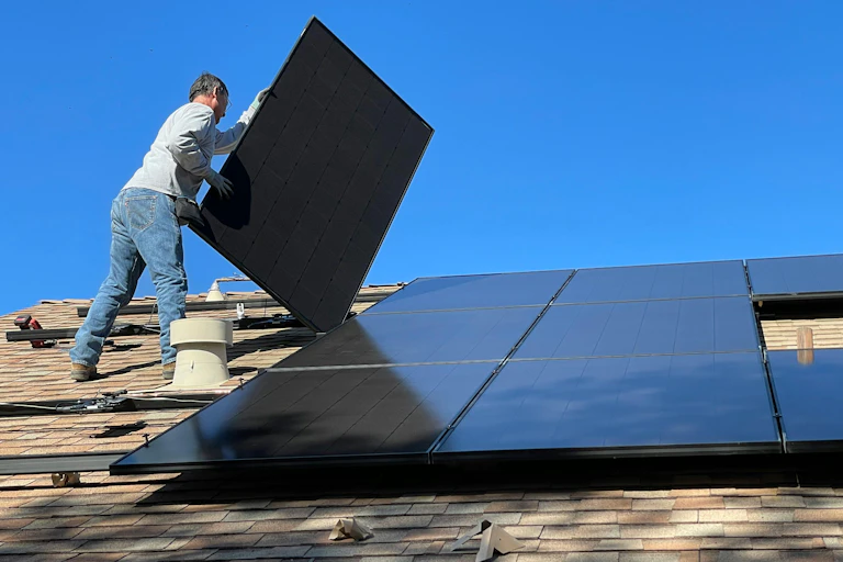 A man installs solar panels on a roof.
