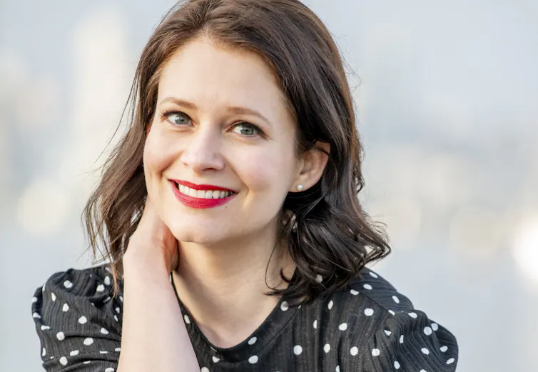 a smiling woman in a polka dot shirt, with red lipstick
