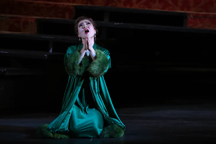 a woman in a green dress singing on her knees, hands clasped