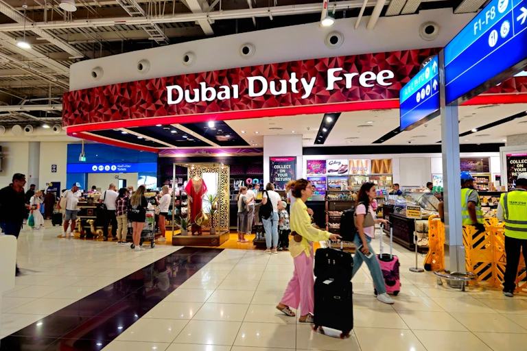 People with suitcases walk in front of a sign that reads "Dubai duty free"