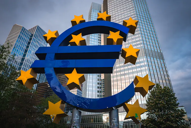 Large structure of the Euro symbol with gold stars and skyscrapers.