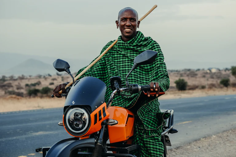 Man in checked shawl, holding a stick and sitting on a motorbike
