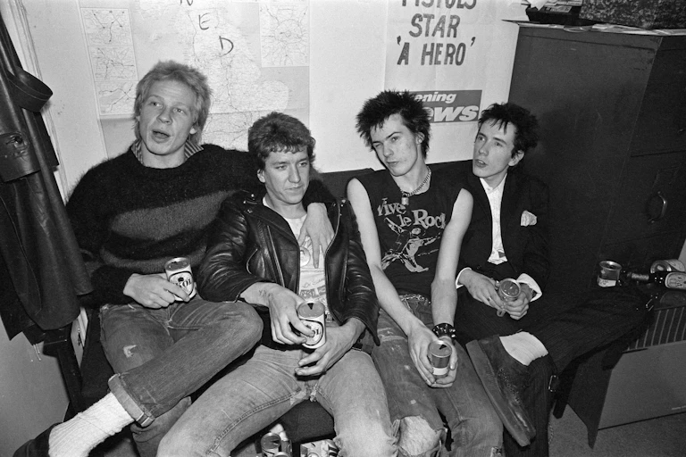 The Sex Pistols backstage, sat on a sofa together drinking beer.