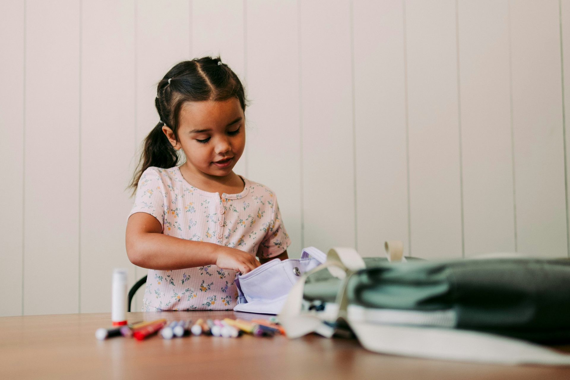 A child at a table looking through some writing utensils and a pencil case. 