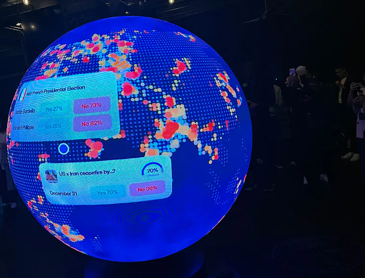 A blue, sphere-shaped LED screen features various trades that can be made through Polymarket.