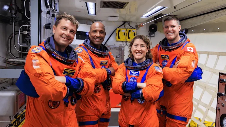 Four astronauts in orange suits. Astronaut Victor Glover