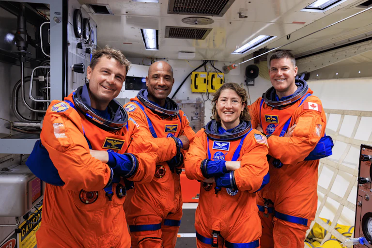 Four astronauts wearing orange jumpsuits