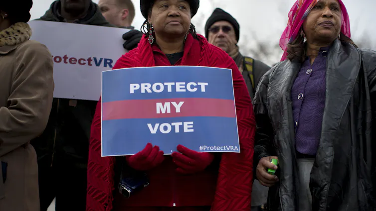 A Black woman holds a poster defending voting rights.