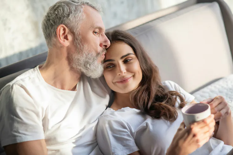 An older man and a younger woman having coffee in bed.