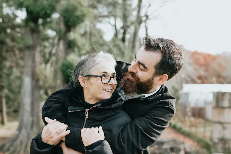 An older woman embracing a younger man outdoors.