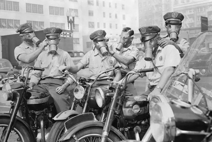 Half a dozen people sitting on motorcycles and wearing gas masks.