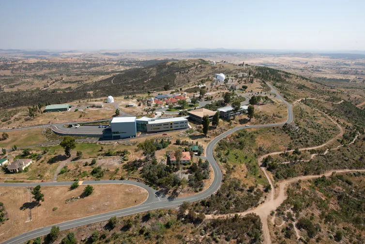 Aerial view of a small observatory on a rugged Australian hill.