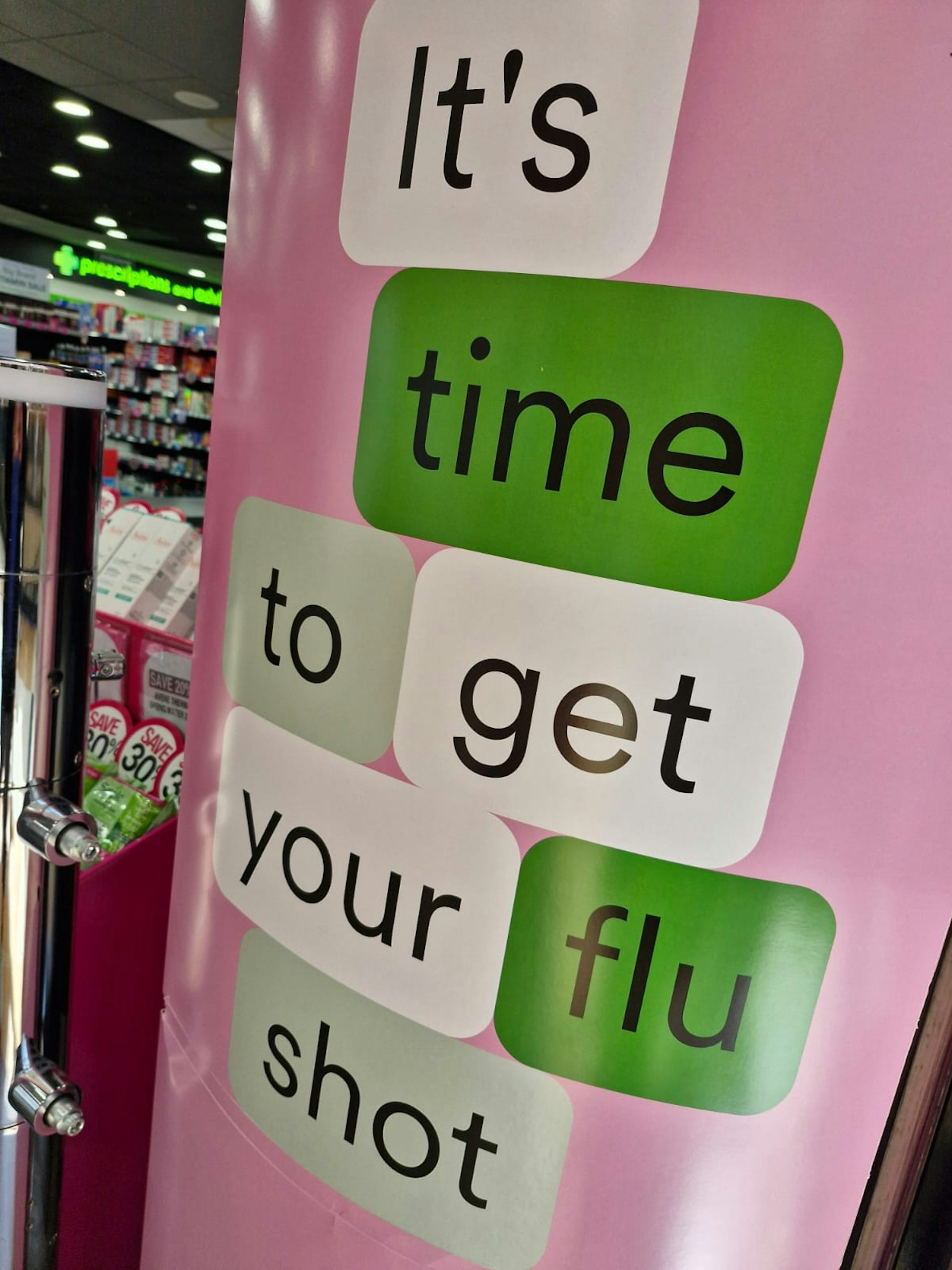 Pink, green and white shop signage says 'It's time to get your flu shot'