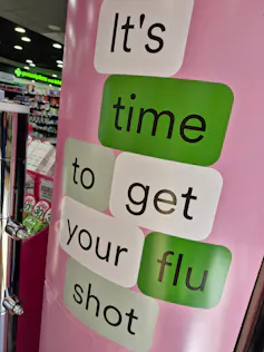 Pink, green and white shop signage says 'It's time to get your flu shot'