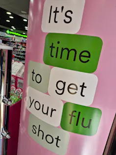 Pink, green and white shop signage says 'It's time to get your flu shot'