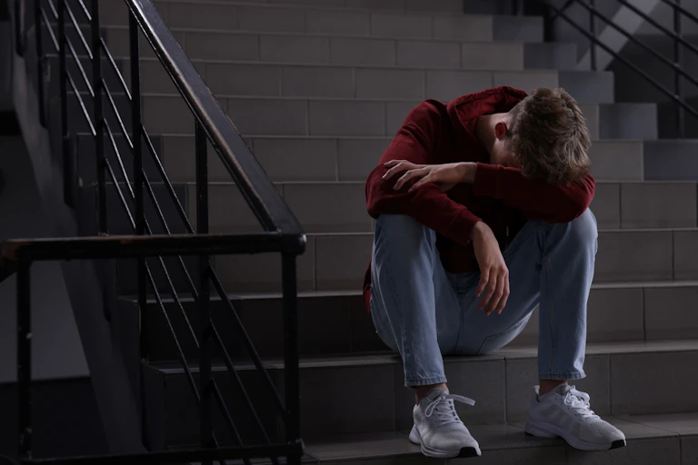 A boy sitting with his head down on school stairs.