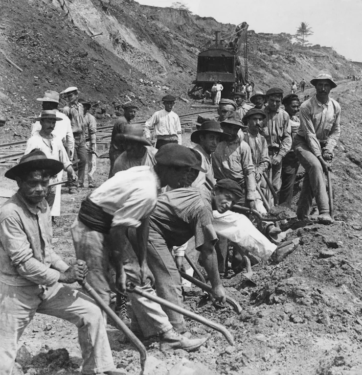 A group of people holding hand tools stand next to a large pile of soil.