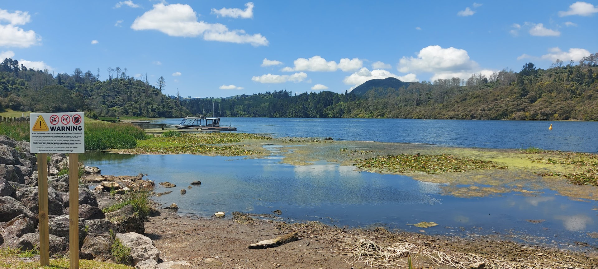 This image shows a green sludge in the Waikato River, with an official warning sign.