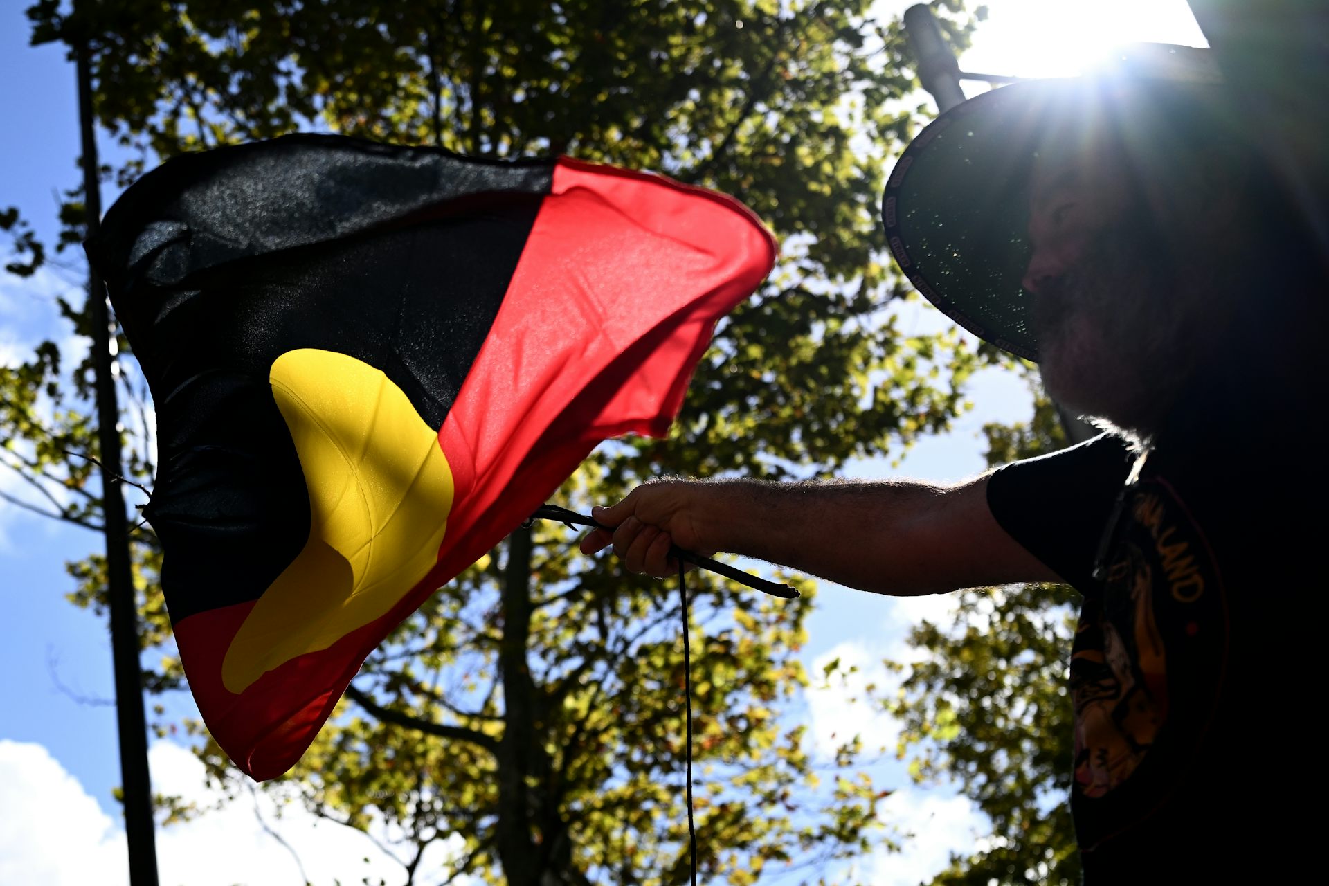 An Aboriginal flag flying in the air against a blue sunny sky.