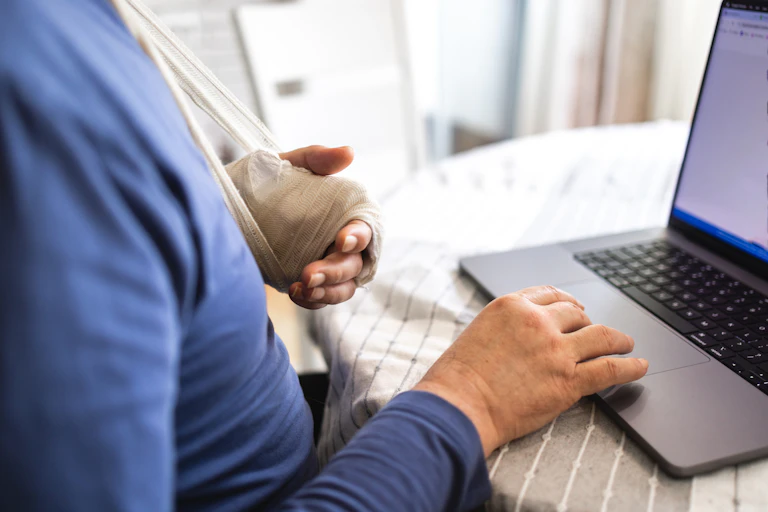Man with left in sling, using right hand to type on laptop