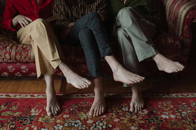 Three people sit on a couch with legs crossed.