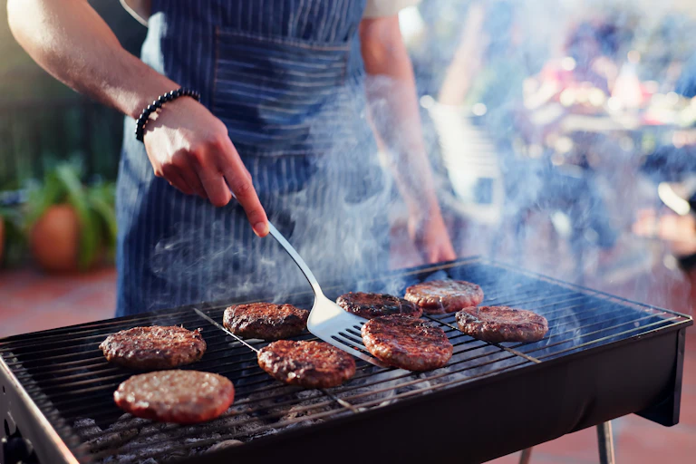 Una persona fent una barbacoa d'hamburgueses.