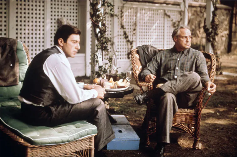 An older man and his son sitting in a garden talking.